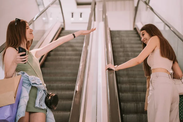Two friends meeting each other in the middle of the escalator in the shopping mall