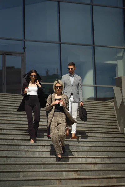 Three well suited business people with sunglasses are walking down the stiars