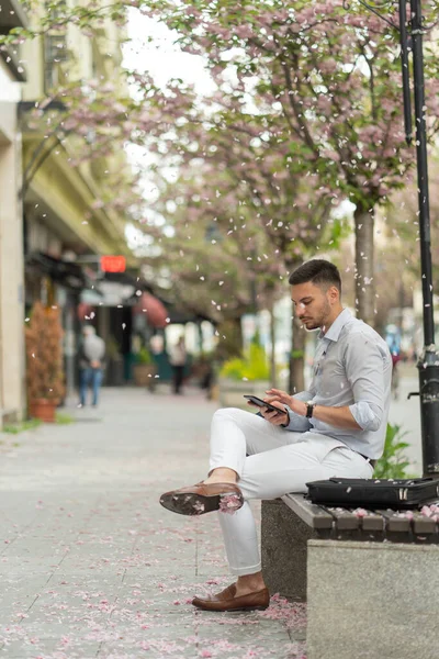 Handsome and urban businessman is working on his tablet while sitting on the bench