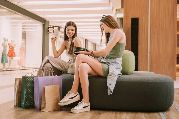 Two Pretty Girls Sitting Sofa Shopping Mall While Looking Black — ストック写真