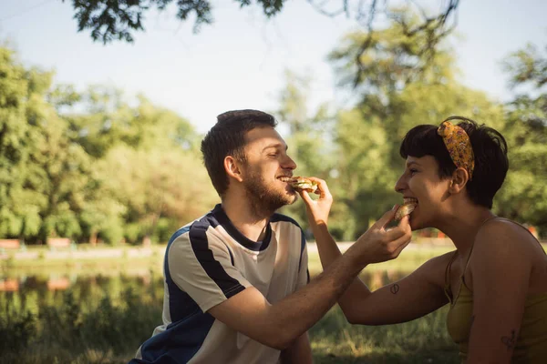 Beautiful couple feeding eachother while sitting on the picnic in the park