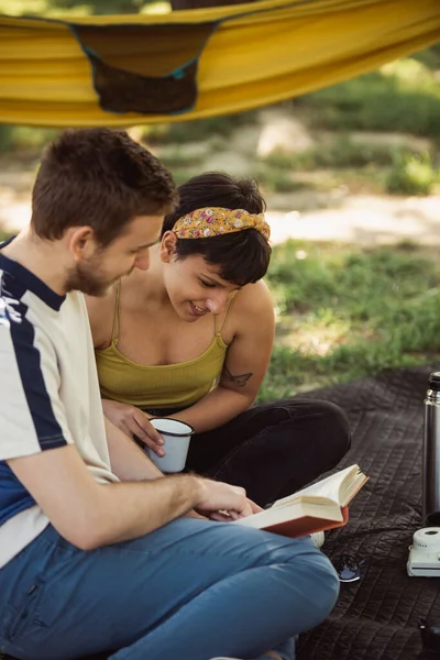Pretty couple reading together while sitting on a picnic in the park