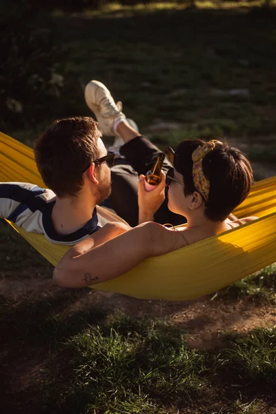 Cool Couple Drinking Beer While Relaxing Yellow Hammock Park — Stockfoto