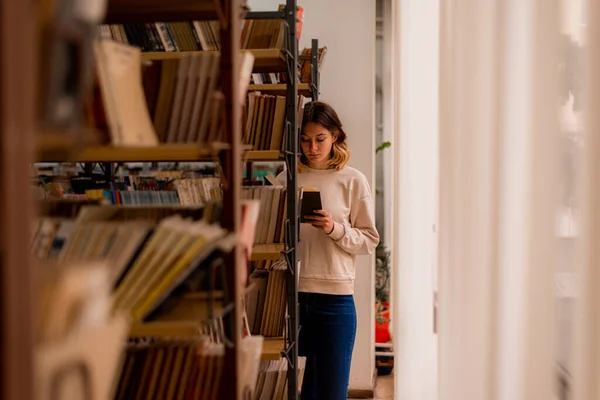 Beautiful Girl Reading Book While Standing Bookshelves — Stok fotoğraf