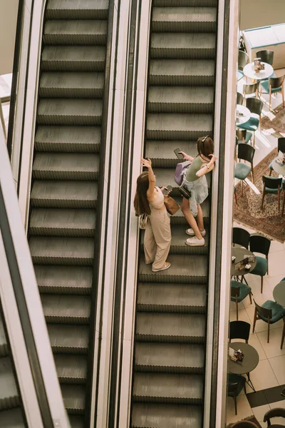 Two Pretty Girls Going Escalator City Mall While Holding Phones — Fotografia de Stock