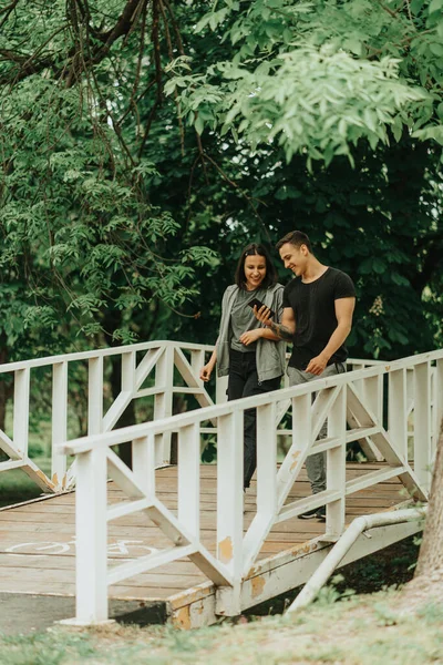 Beautiful Couple Laughing Looking Phone While Walking White Bridge Park — Stockfoto