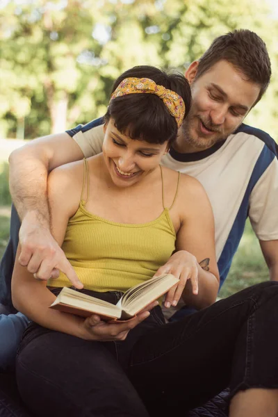 Amazing couple looking at the book while sitting on a picnic in the park