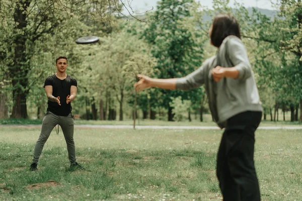 Sport girl throwing frisbee to her boyfriend while standing in the park