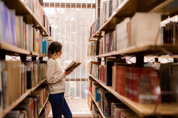 Linda Chica Leyendo Libro Mientras Está Pie Entre Los Estantes — Foto de Stock