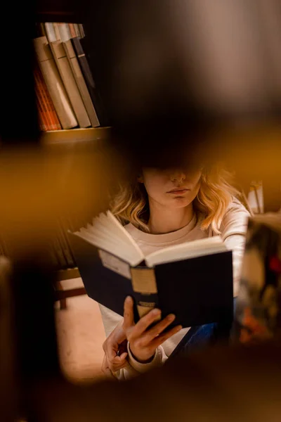 Κορίτσι Ανάγνωση Μεταξύ Των Βιβλιοθηκών Μια Βιβλιοθήκη Ενώ Κάθεται — Φωτογραφία Αρχείου