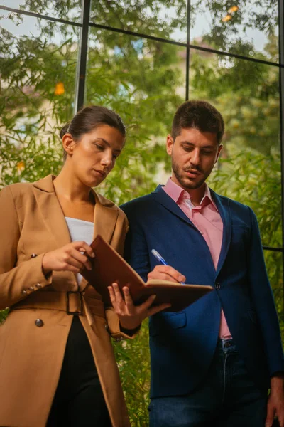 Hombre Negocios Está Escribiendo Cuaderno Mientras Compañera Sostiene —  Fotos de Stock