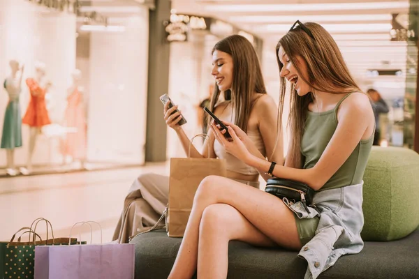 Twee Leuke Meisjes Kijken Naar Hun Telefoons Terwijl Bank Zitten — Stockfoto