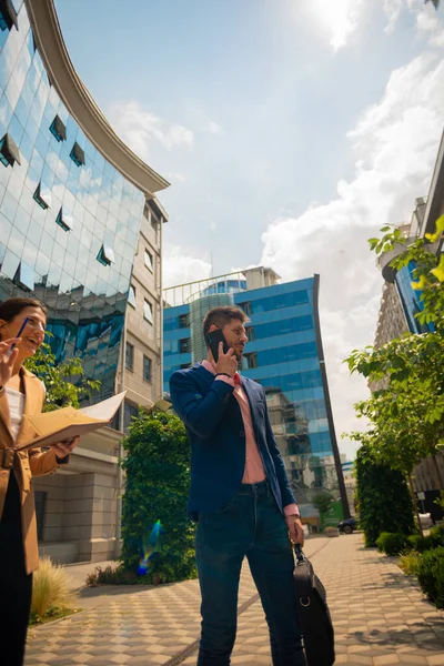 A male businessman is consulting with his boss on mobile while his female partner is laughing at something