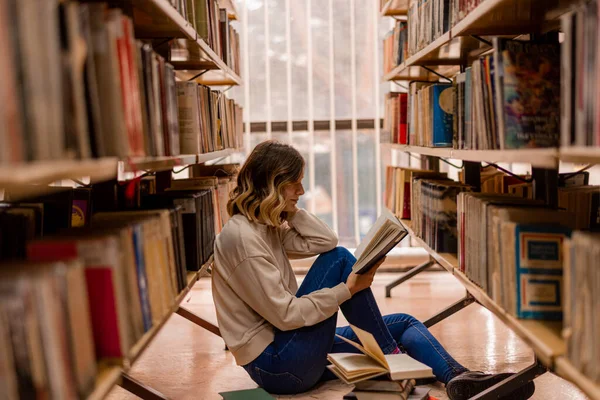 Dziewczyna Myśli Czyta Siedząc Bibliotece Między Regałami — Zdjęcie stockowe