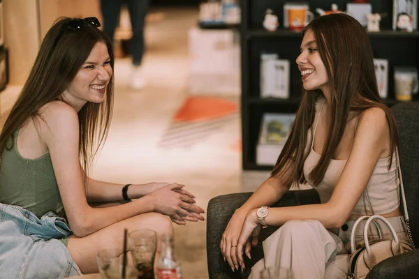 两个漂亮的姑娘坐在商场的咖啡店里笑着 — 图库照片