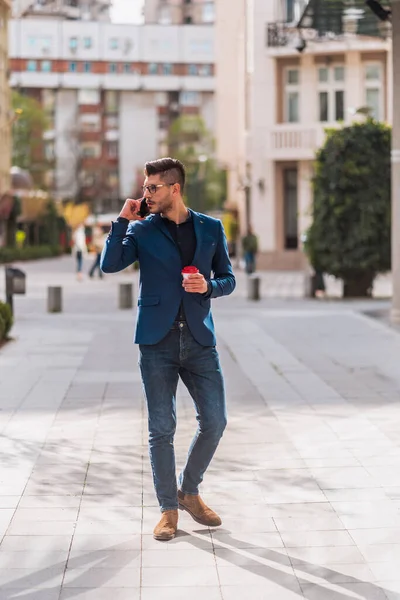 Young urban businessman professionaldrinking coffe to go and talking on smartphone