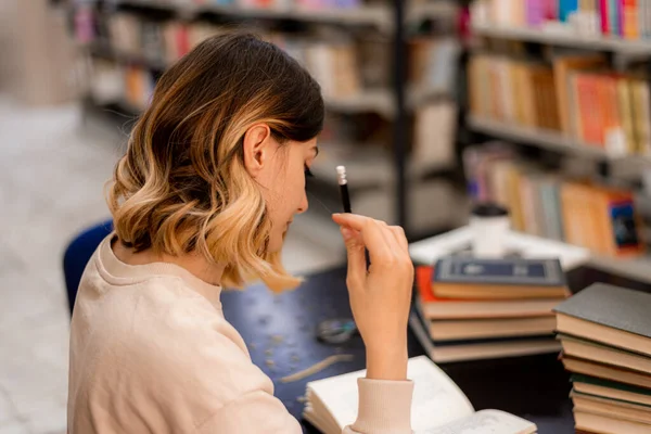美しい少女は鉛筆を持って図書館で本を読みながら集中しようとします — ストック写真