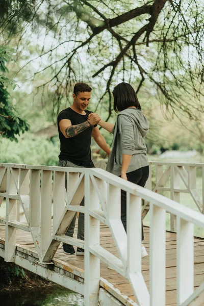 在公园的白桥上 这对神奇的情侣一边站着一边握手一边笑 — 图库照片