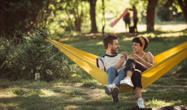 Ładna Para Relaksująca Się Żółtym Hamaku Parku Podczas Wspólnych Kanapek — Zdjęcie stockowe