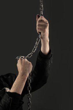 Siyah arka planda demir zincirlerle birbirine dolanmış eller. Kavram