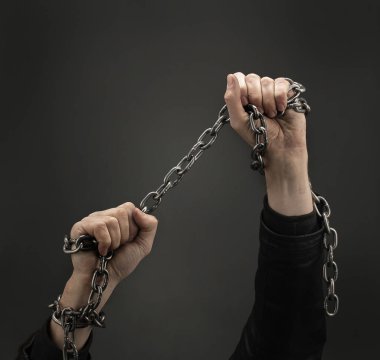 Siyah arka planda demir zincirlerle birbirine dolanmış eller. Kavram