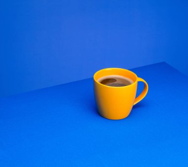 Sarı kahve fincanı mavi arka planda mavi bir masanın üzerinde duruyor. Minimalizm kavramı. Metin için yer