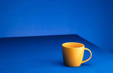 Sarı kahve fincanı mavi arka planda mavi bir masanın üzerinde duruyor. Minimalizm kavramı. Metin için yer