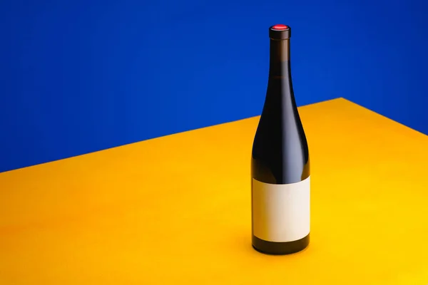 青い背景に黄色のテーブルの上にワインのボトル ミニマリズムの概念 広告用ポスター テキストの場所 — ストック写真