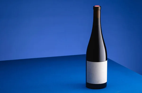 青い背景の青いテーブルの上にワインのボトル ミニマリズムの概念 広告用ポスター テキストの場所 — ストック写真