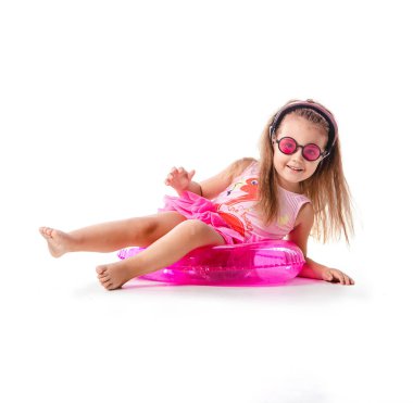 Mutlu pozitif küçük kız şişme yüzme yüzüğüyle duruyor pembe mayo ve güneş gözlüğü takıyor beyaz arka planda izole bir şekilde yüzmeye hazır..