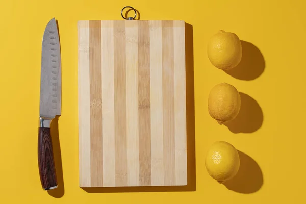 Chef\'s Knife with yellow lemons and a cutting board on a yellow background. The concept of minimalism