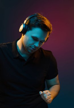 Kırmızı stüdyo arka planında turuncu renkli neonlu yakışıklı ve duygusal bir adamın portresi. Zevkle ve kulaklıkla müzik dinlemek. Broşür Posteri ReklamcıIığı