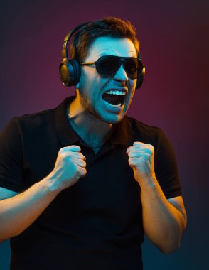 Yakışıklı, genç, duygusal bir adamın portresi portakal renkli neon. Çok duygusal bir şekilde kulaklıkla müzik dinliyor, güneş gözlüğü takıyor, ağzını açıyor, yumruklarını kenetleyerek ellerini kaldırıyor. Broşür Posteri ReklamcıIığı