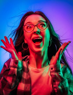 Çok renkli arka planda, neon ışıklarda genç duygusal kadın portreleri. Neşeli bir sürpriz ve açık bir ağızla. Mesaj için yer. Broşür Posteri Afişi