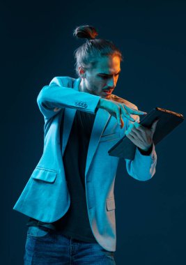 Koyu mavi arka planda elektronik tablet ve kalemle duygusal genç ve yakışıklı bir tasarımcı.