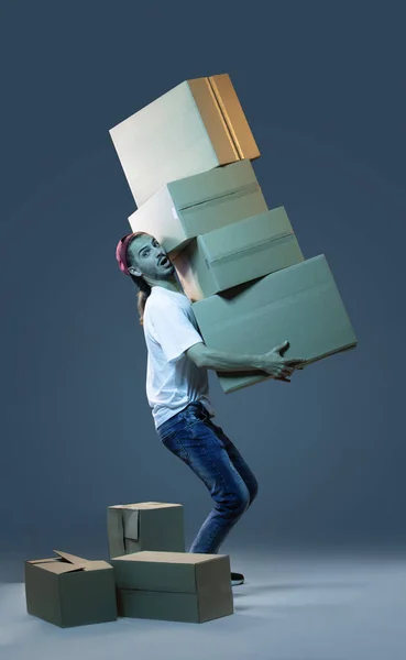 Emotional delivery guy with a lot of boxes on a dark blue background