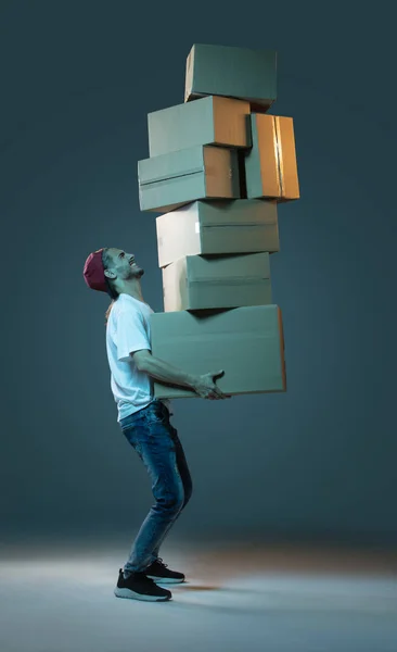 Emotional delivery guy with a lot of boxes on a dark blue background