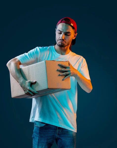 Emotional delivery guy with a lot of boxes on a dark blue background