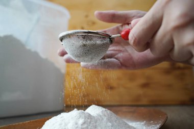 Bir kadın elinde unla süzgeç tutuyor..