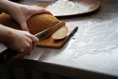 Bir kadın masada bir somun ekmek kesiyor..