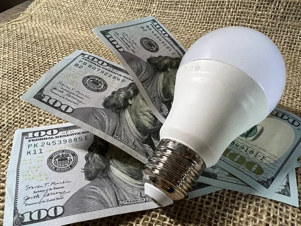 A light bulb and dollar bills on the table.