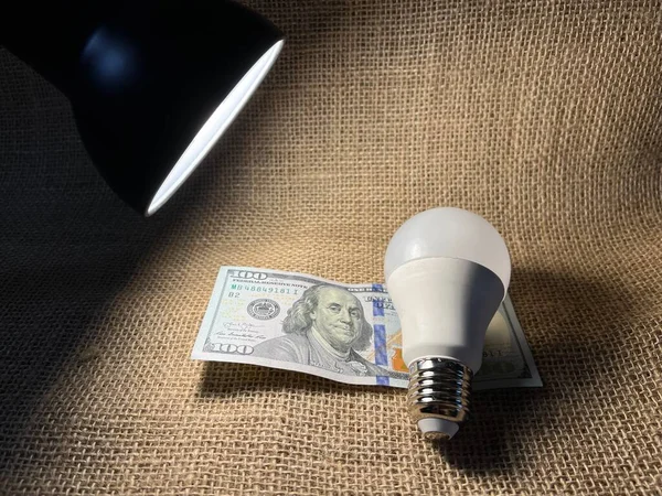 A light bulb and dollar bills on the table.