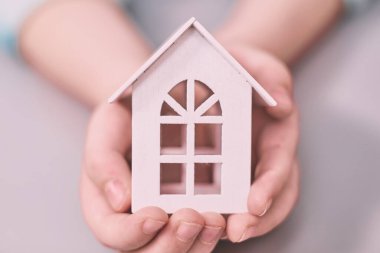 Bir ev modeline el ele tutuşmak. Ev alma ve kiralama konsepti. Gri arkaplan.