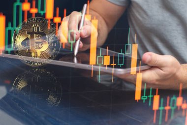 Man Bitcoin ticaret şeması ekranda. Elinde altın bir Bitcoin nakit para tutuyor. Kripto para değişimi ticareti..
