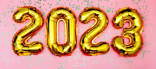 2023 golden foil balloons numbers,  stars confetti, ribbons and bokeh. Top horizontal view copy space new year and holiday concept.