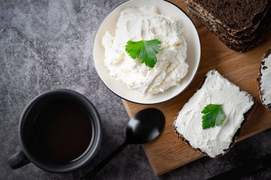 Çavdar ekmeği, kaymak peyniri, ricotta ve bitkilerle ahşap kesim tahtasının üzerinde. Yeşil otlarla süslenmiş.