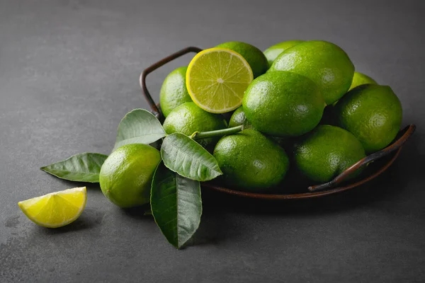 Verse groene limoenen met bladeren op grijze stenen tafel — Stockfoto