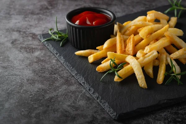 Homemade baked french fries with ketchup and rosemary on a black slate board — Stock Photo, Image