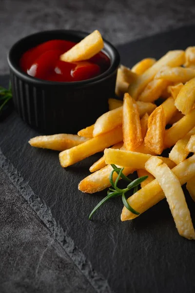 Домашняя выпечка картошки фри с кетчупом и розмарином на черной доске — стоковое фото