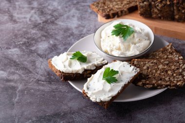 Çavdar ekmeği ahşap bir kesim tahtasının üzerinde peynir, ricotta ve otlarla..